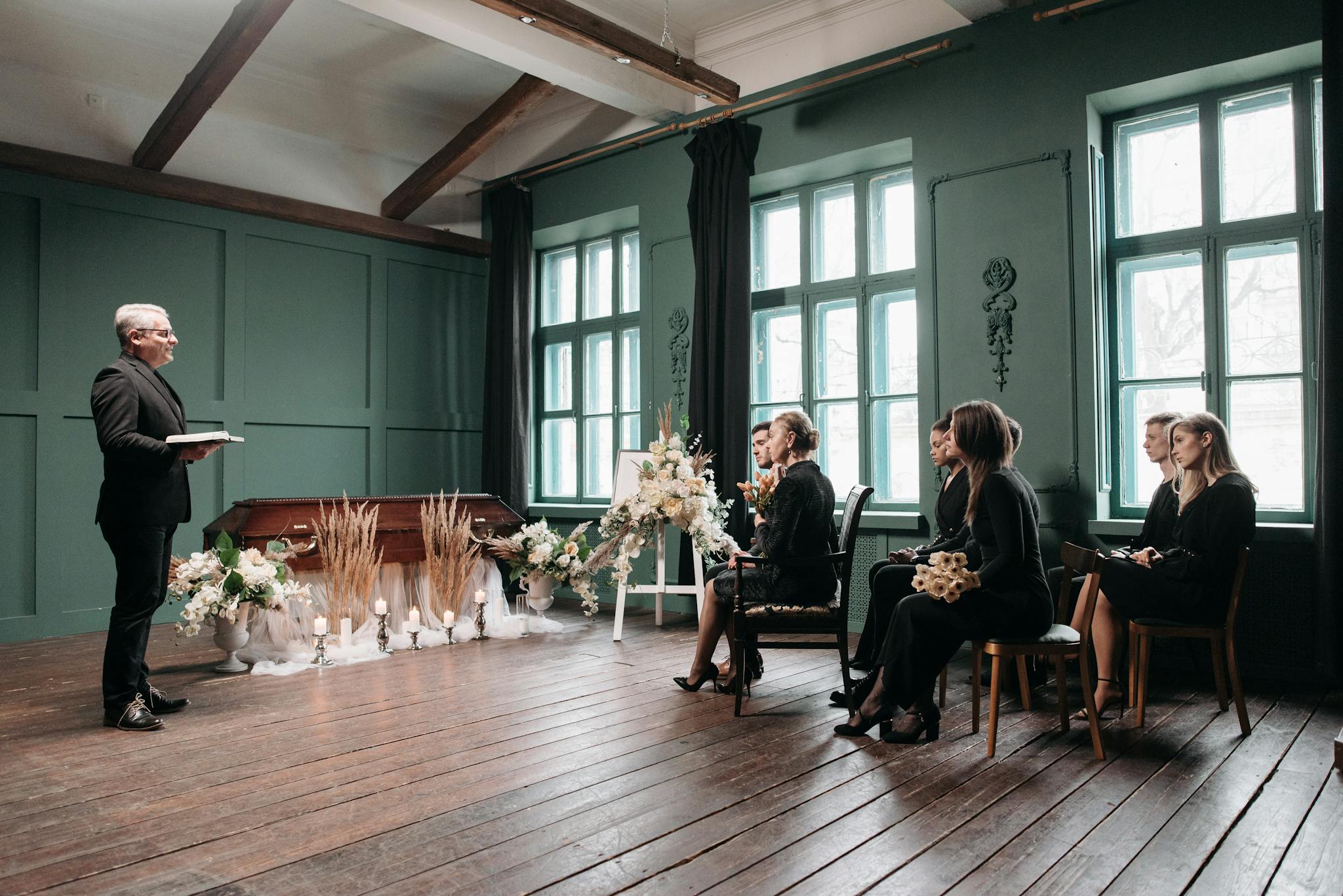 A peaceful indoor funeral ceremony scene with a pastor and seated mourners.